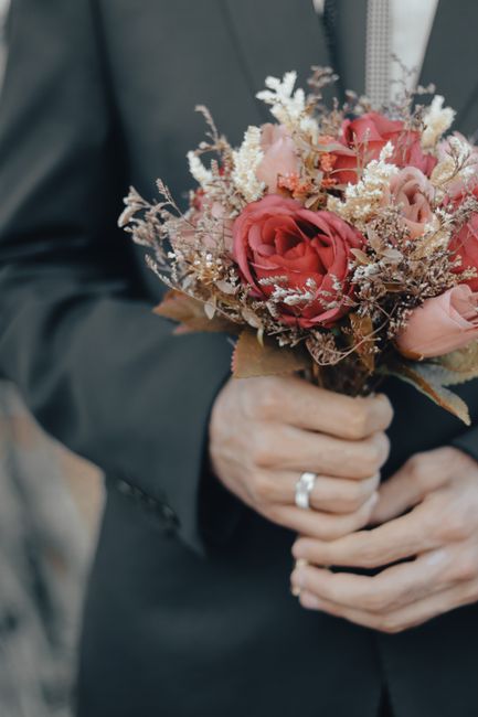 A bouquet of fresh flowers resting on the hood of a turquoise car, featuring pink lilies, white roses, pink gerbera daisies, and purple roses, accented with sprigs of baby's breath and large dark gree